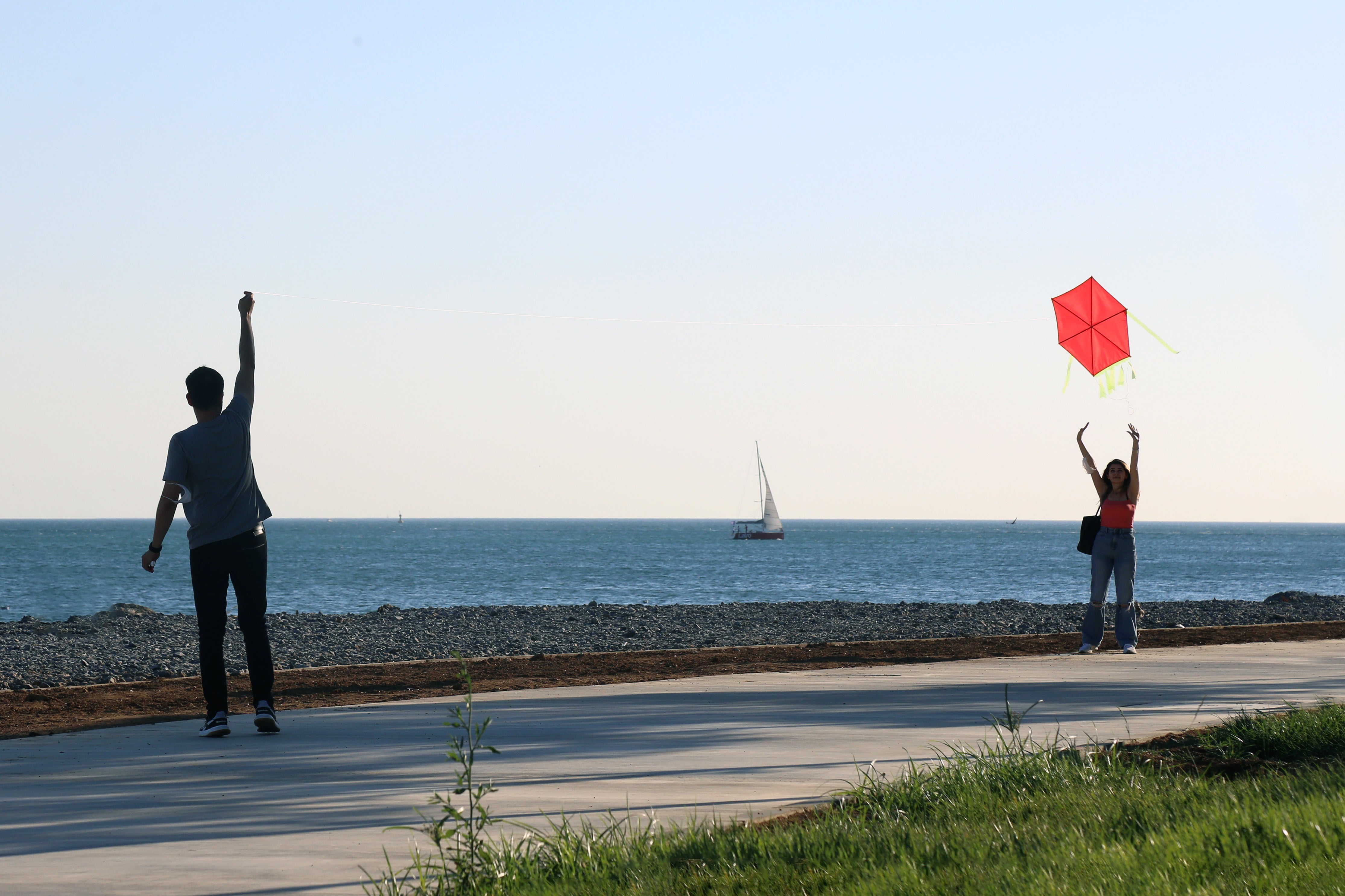 Two people trying to fly a red kite by the water